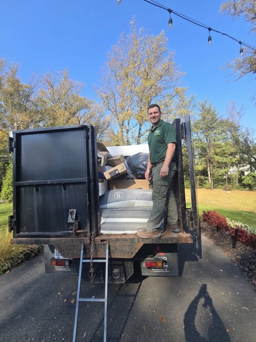 Wee Haul junk removal crew member standing in the company truck, loaded with a mattress, boxes, and bagged junk from a residential pickup