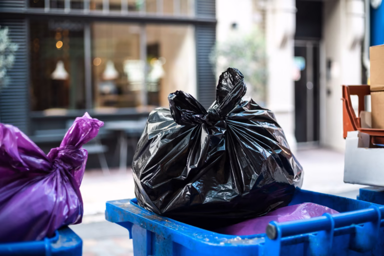 Purple and black bags of trash on a garbage bin during daytime